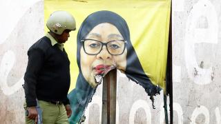 A Tanzanian riot police officer walks past a vandalized campaign sign for President Samia Suluhu.