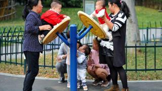 Three women play with several small children in a park.
